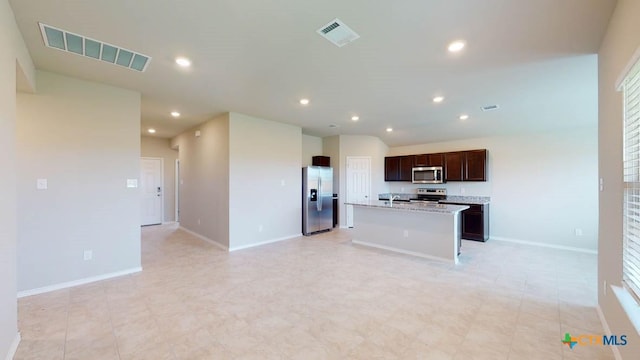 kitchen with stainless steel appliances, light stone countertops, a kitchen island with sink, and dark brown cabinetry