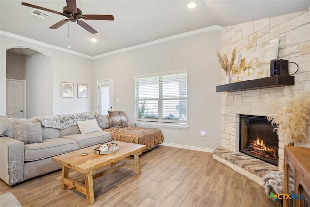 living area featuring visible vents, ornamental molding, arched walkways, a fireplace, and light wood finished floors