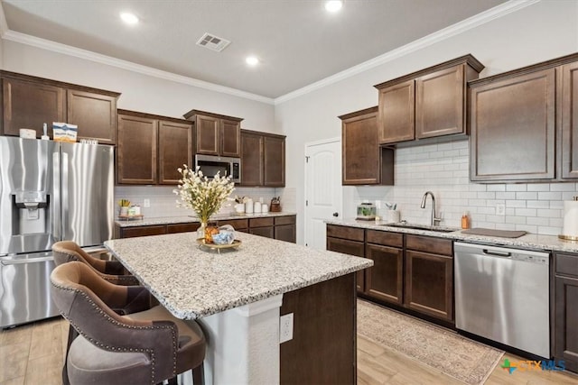 kitchen with light stone countertops, a kitchen island, a sink, dark brown cabinets, and appliances with stainless steel finishes