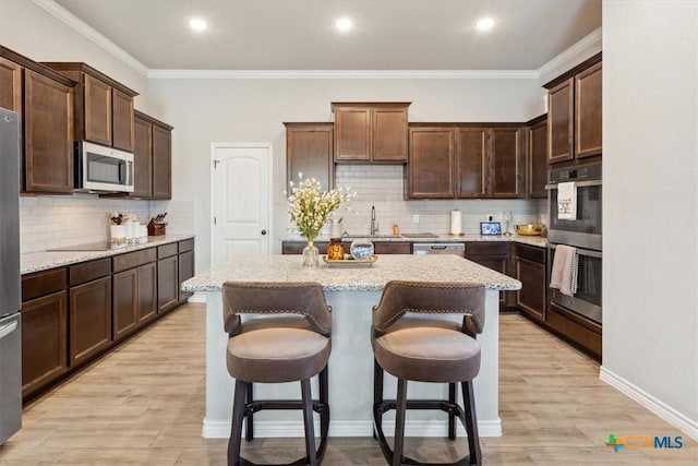 kitchen featuring light wood finished floors, dark brown cabinetry, appliances with stainless steel finishes, a kitchen breakfast bar, and a center island