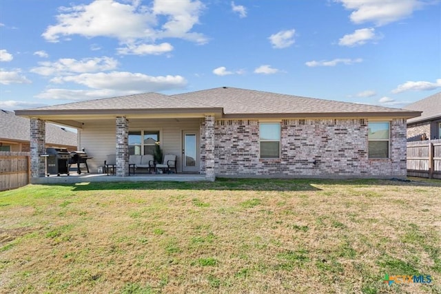 rear view of property featuring brick siding, a patio, fence, and a lawn