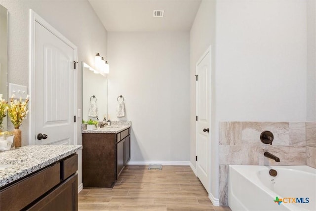 full bath with visible vents, a garden tub, wood finished floors, baseboards, and vanity