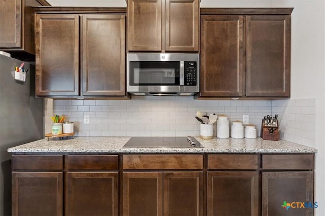 kitchen with light stone counters, dark brown cabinets, backsplash, and stainless steel appliances