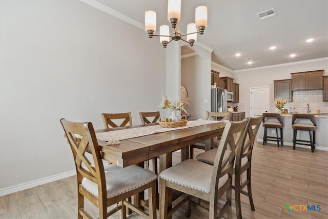 dining area featuring an inviting chandelier, crown molding, light wood-style floors, and visible vents