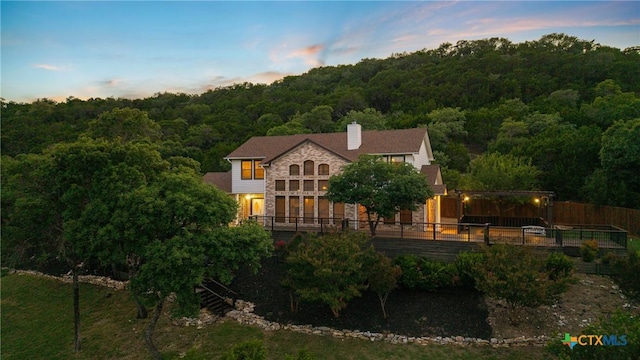 3614 Quail Hollow Rd, Harker Heights, TX 76548 - back of property at dusk with a wooded view, a chimney, a wooden deck, and stone siding