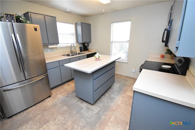kitchen with a sink, gray cabinetry, light countertops, a kitchen island, and appliances with stainless steel finishes