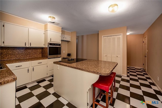 kitchen featuring black electric cooktop, stainless steel oven, dark countertops, decorative backsplash, and light floors