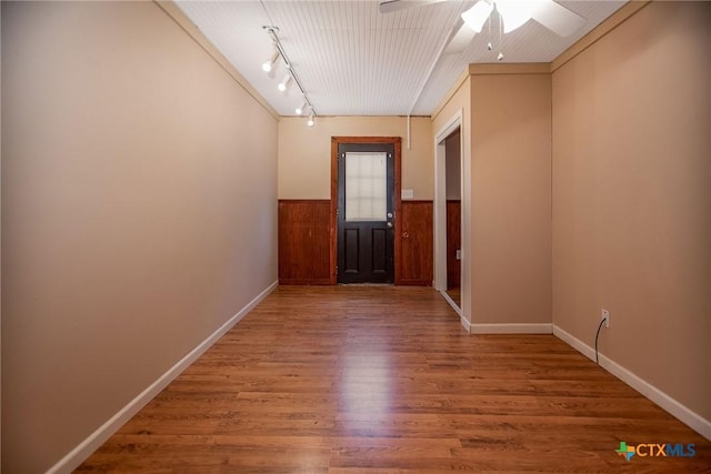 spare room featuring track lighting, wood finished floors, baseboards, wainscoting, and ceiling fan