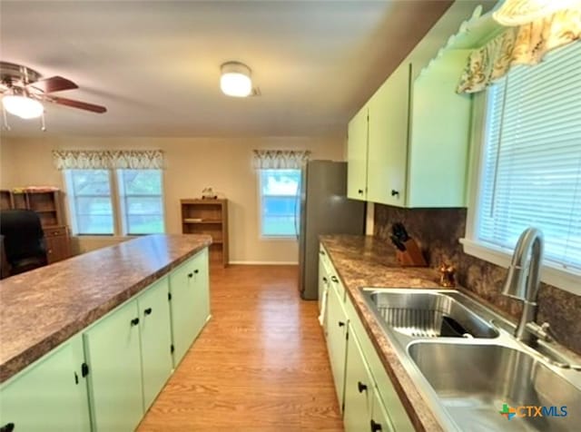 kitchen featuring sink, green cabinetry, light hardwood / wood-style flooring, stainless steel fridge, and decorative backsplash