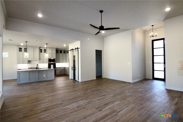 unfurnished living room with a barn door, crown molding, and dark hardwood / wood-style flooring