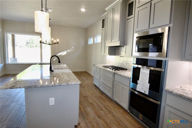 kitchen featuring appliances with stainless steel finishes, a kitchen island with sink, sink, decorative light fixtures, and light hardwood / wood-style flooring