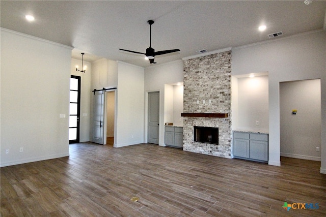 unfurnished living room with a fireplace, hardwood / wood-style floors, a barn door, and ceiling fan