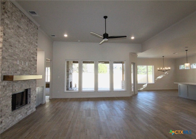 unfurnished living room with a wealth of natural light, a fireplace, ceiling fan with notable chandelier, and dark hardwood / wood-style floors