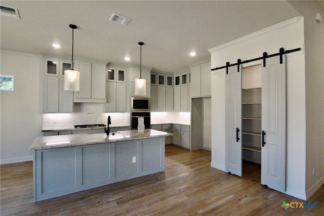 kitchen with light wood-type flooring, light stone counters, a center island with sink, oven, and stainless steel microwave