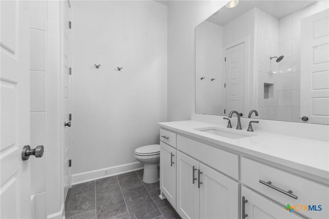 bathroom with toilet, tiled shower, vanity, and baseboards