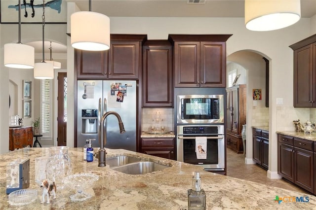 1919 Los Santos Dr, San Marcos, TX 78666 - kitchen featuring tasteful backsplash, arched walkways, light stone counters, hanging light fixtures, and stainless steel appliances