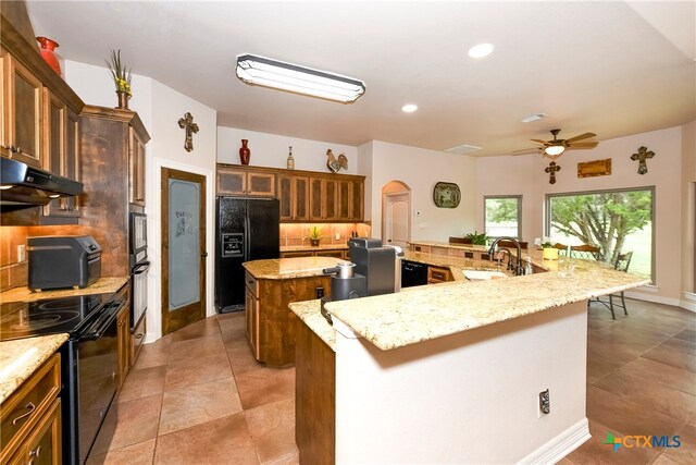 kitchen featuring black appliances, decorative backsplash, sink, ceiling fan, and a spacious island