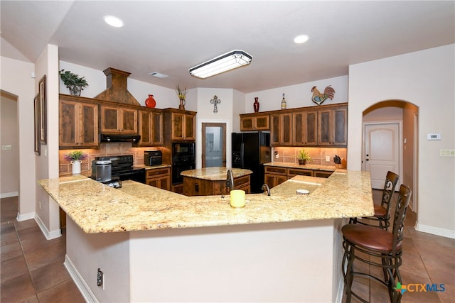 kitchen featuring black appliances, light stone counters, backsplash, a breakfast bar area, and a spacious island