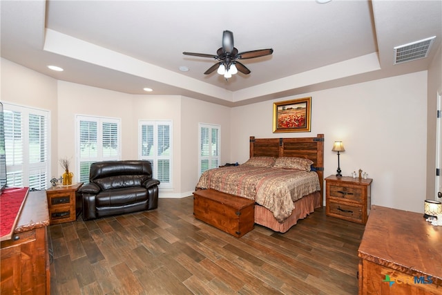 bedroom featuring dark wood-type flooring, ceiling fan, multiple windows, and a raised ceiling