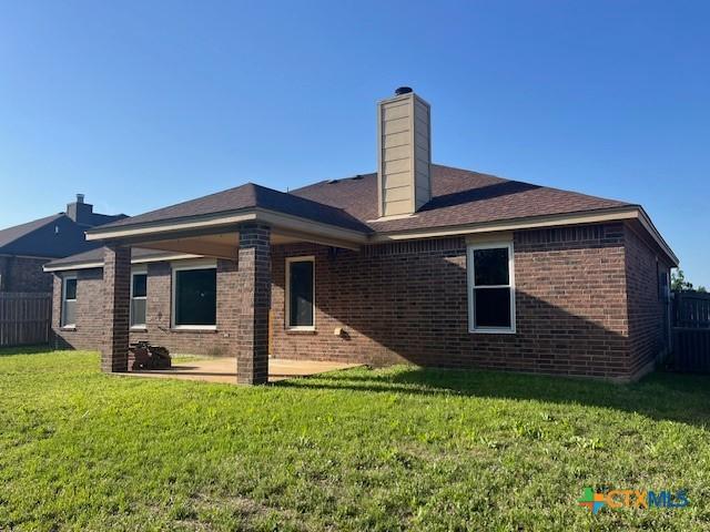 back of house featuring a yard, a patio, fence, brick siding, and a chimney