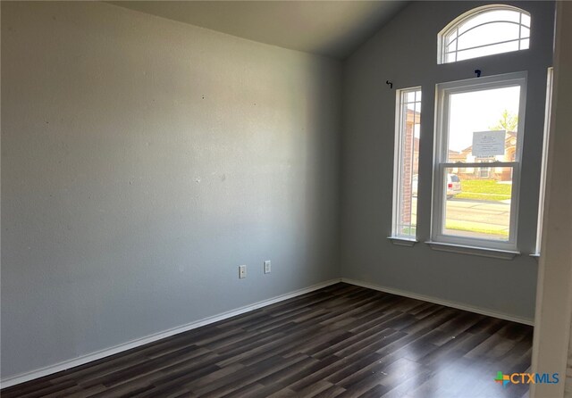 empty room with baseboards, vaulted ceiling, and dark wood finished floors