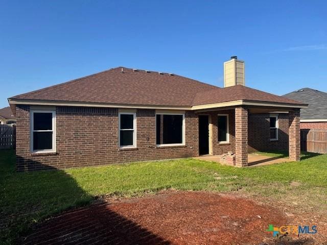 rear view of property featuring a lawn, a patio, fence, brick siding, and a chimney