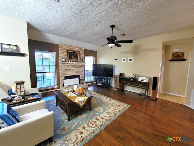 living room featuring ceiling fan, a fireplace, a textured ceiling, and dark wood-type flooring