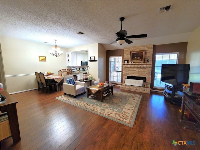 living room featuring dark hardwood / wood-style flooring, a textured ceiling, ceiling fan with notable chandelier, a fireplace, and plenty of natural light