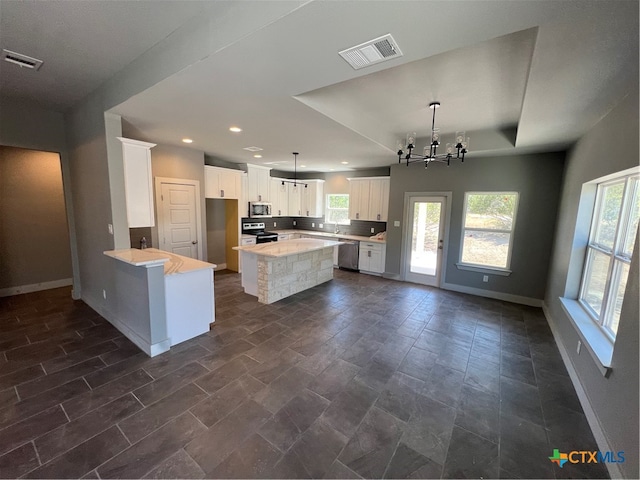 kitchen featuring stainless steel appliances, white cabinetry, a notable chandelier, kitchen peninsula, and a center island