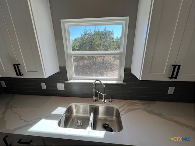 kitchen featuring tasteful backsplash, white cabinetry, sink, and light stone counters