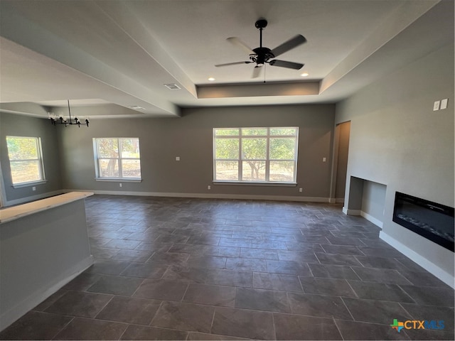 unfurnished living room with ceiling fan with notable chandelier and a tray ceiling