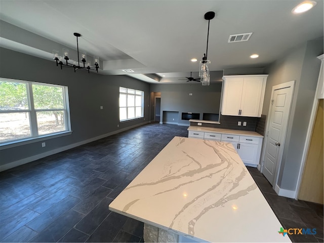 kitchen featuring pendant lighting, ceiling fan with notable chandelier, light stone counters, and white cabinets