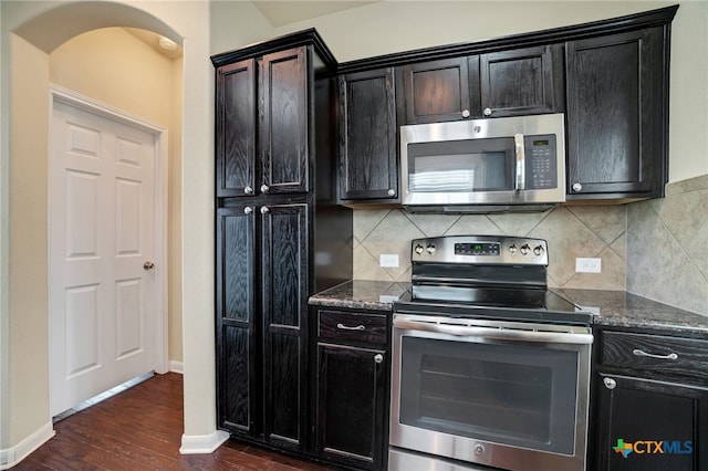 kitchen featuring stainless steel appliances, dark stone countertops, decorative backsplash, and dark hardwood / wood-style flooring