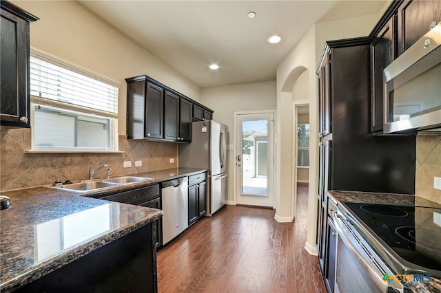 kitchen featuring stainless steel appliances, dark hardwood / wood-style flooring, dark stone counters, sink, and backsplash