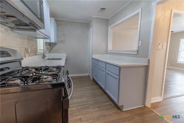 kitchen featuring hardwood / wood-style floors, range with gas stovetop, tile walls, and sink