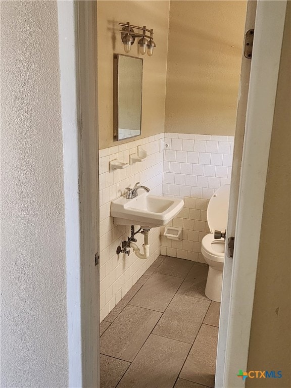 bathroom featuring tile walls, toilet, wainscoting, a sink, and tile patterned flooring