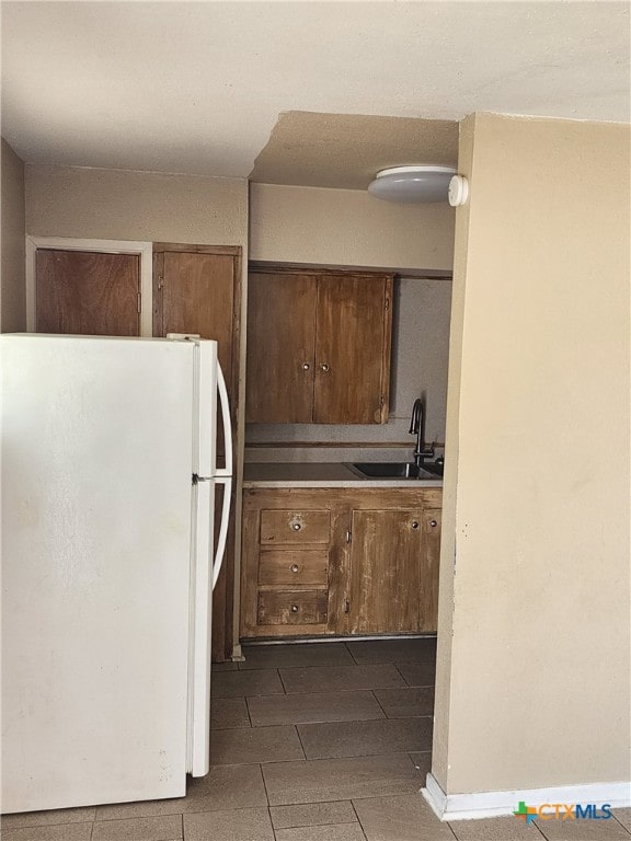 kitchen with baseboards, brown cabinetry, freestanding refrigerator, light countertops, and a sink