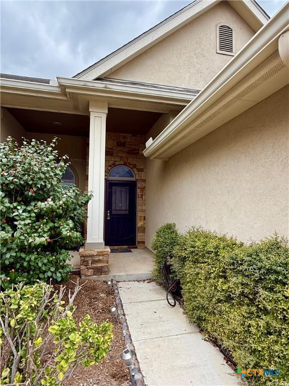 entrance to property with stone siding, visible vents, and stucco siding