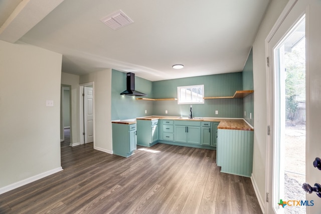 kitchen with dark wood-type flooring, butcher block countertops, wall chimney range hood, and a wealth of natural light