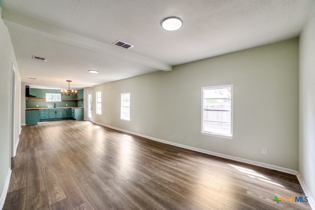 unfurnished living room with dark wood-type flooring, beamed ceiling, a textured ceiling, and a notable chandelier