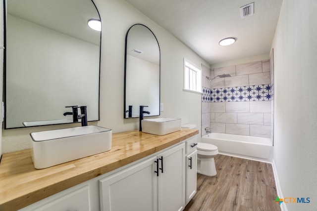 full bathroom featuring hardwood / wood-style floors, vanity, toilet, and tiled shower / bath combo