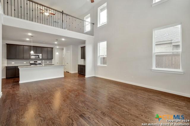 2675 Greenwell Ln, New Braunfels, TX 78130 - unfurnished living room with a ceiling fan, plenty of natural light, a towering ceiling, dark wood finished floors, and baseboards