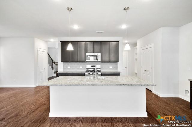 2675 Greenwell Ln, New Braunfels, TX 78130 - kitchen with tasteful backsplash, light stone counters, a kitchen island with sink, dark wood finished floors, and appliances with stainless steel finishes