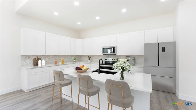 kitchen with a kitchen island with sink, stainless steel appliances, sink, light hardwood / wood-style flooring, and white cabinetry