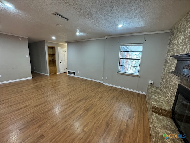 unfurnished living room with wood-type flooring, a textured ceiling, a brick fireplace, and ornamental molding