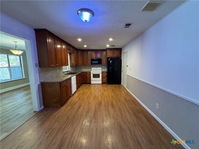 kitchen featuring light stone counters, light hardwood / wood-style flooring, backsplash, a textured ceiling, and white appliances