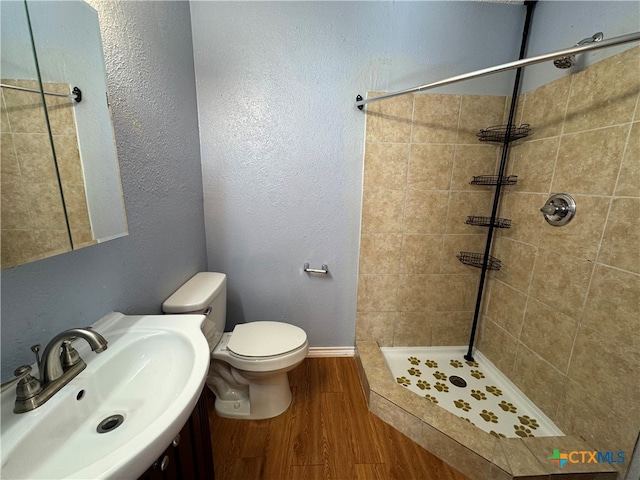 bathroom with tiled shower, toilet, sink, and hardwood / wood-style flooring