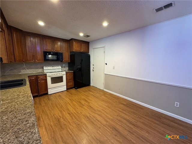 kitchen featuring decorative backsplash, a textured ceiling, black appliances, stone countertops, and hardwood / wood-style flooring