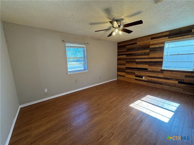 empty room featuring a textured ceiling, dark hardwood / wood-style floors, ceiling fan, and wooden walls