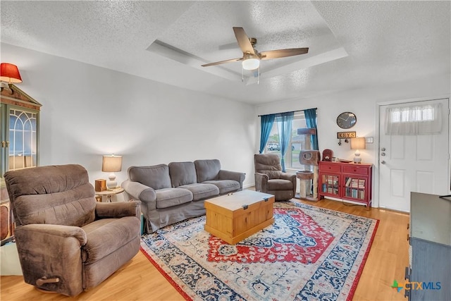 living room with a raised ceiling, a textured ceiling, ceiling fan, and wood finished floors